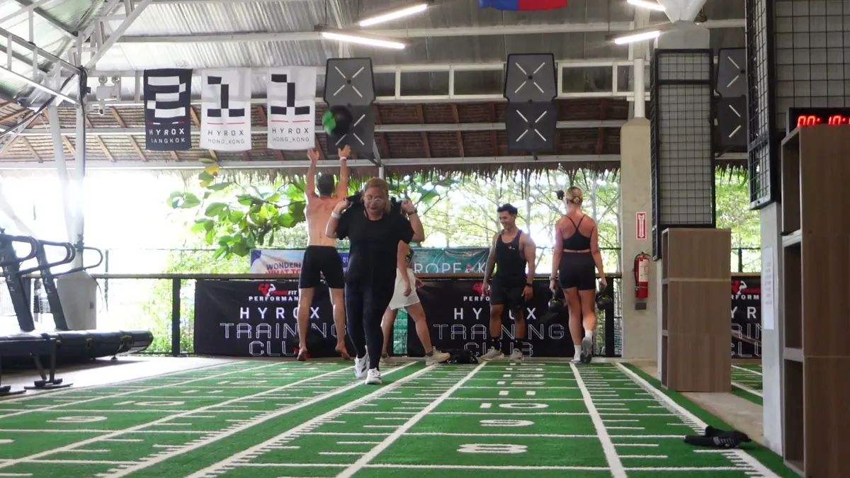 A group standing on a green turf lane under Hyrox banners