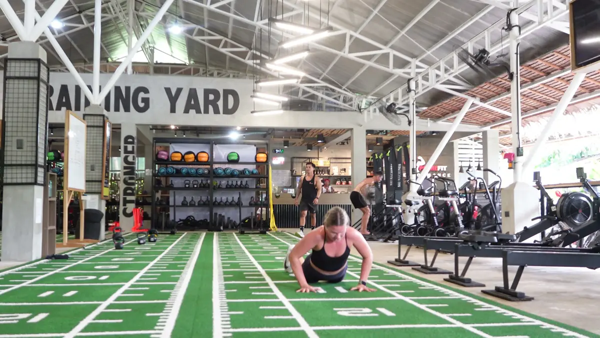 Wide view of a covered gym yard with turf lanes, racks and weights