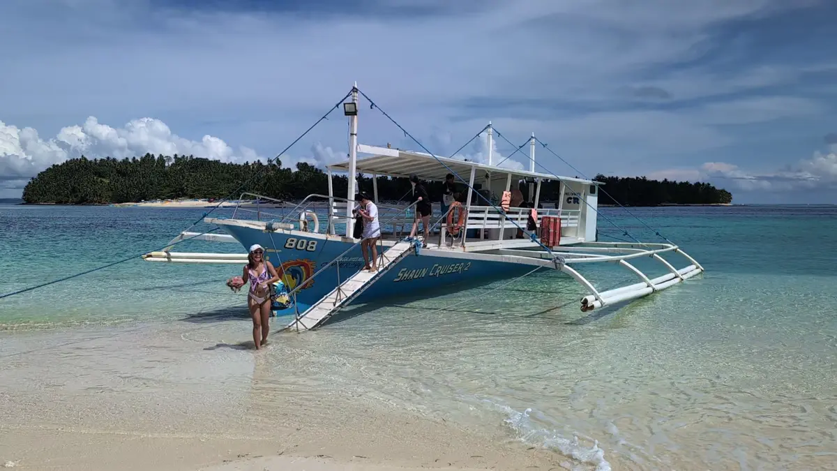 A boat on the shore of a white-sand beach with an island behind it
