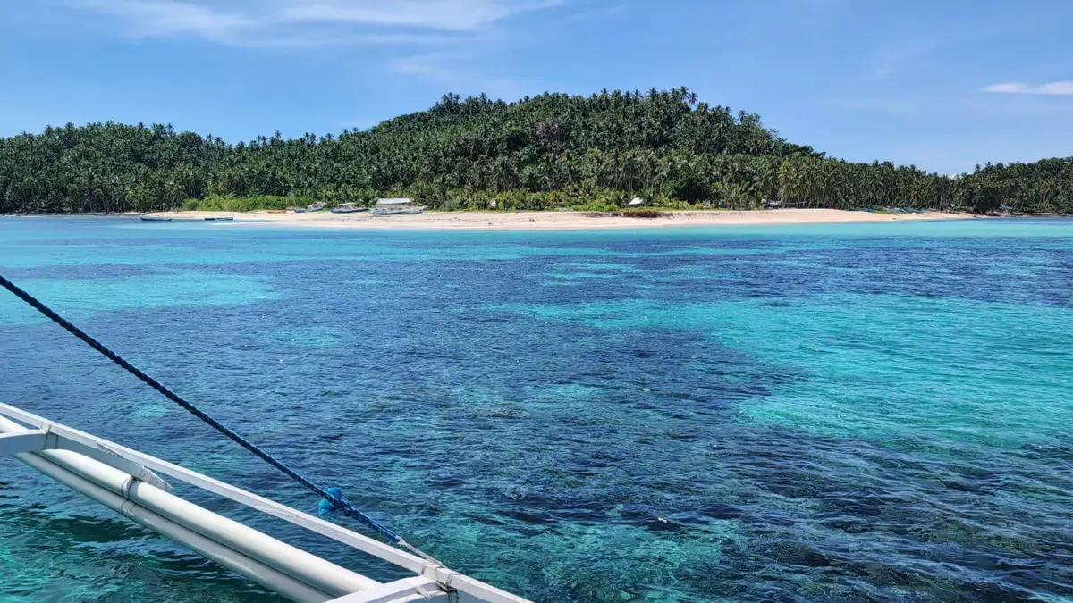 Turquoise water over a reef with a green island on the horizon